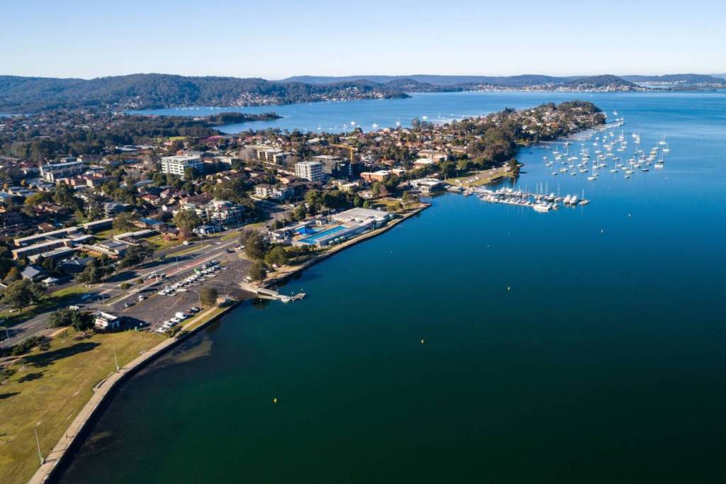 Aerial view of Gosford's waterfront on the Central Coast, with blue waters, moored boats, surrounding neighbourhoods and forested hills