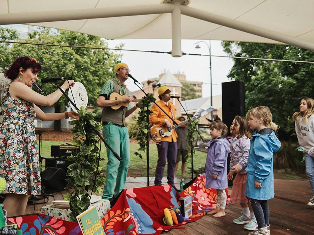 Colourfully dressed musicians performing outdoors for a group of children at a family-friendly festival in Gosford