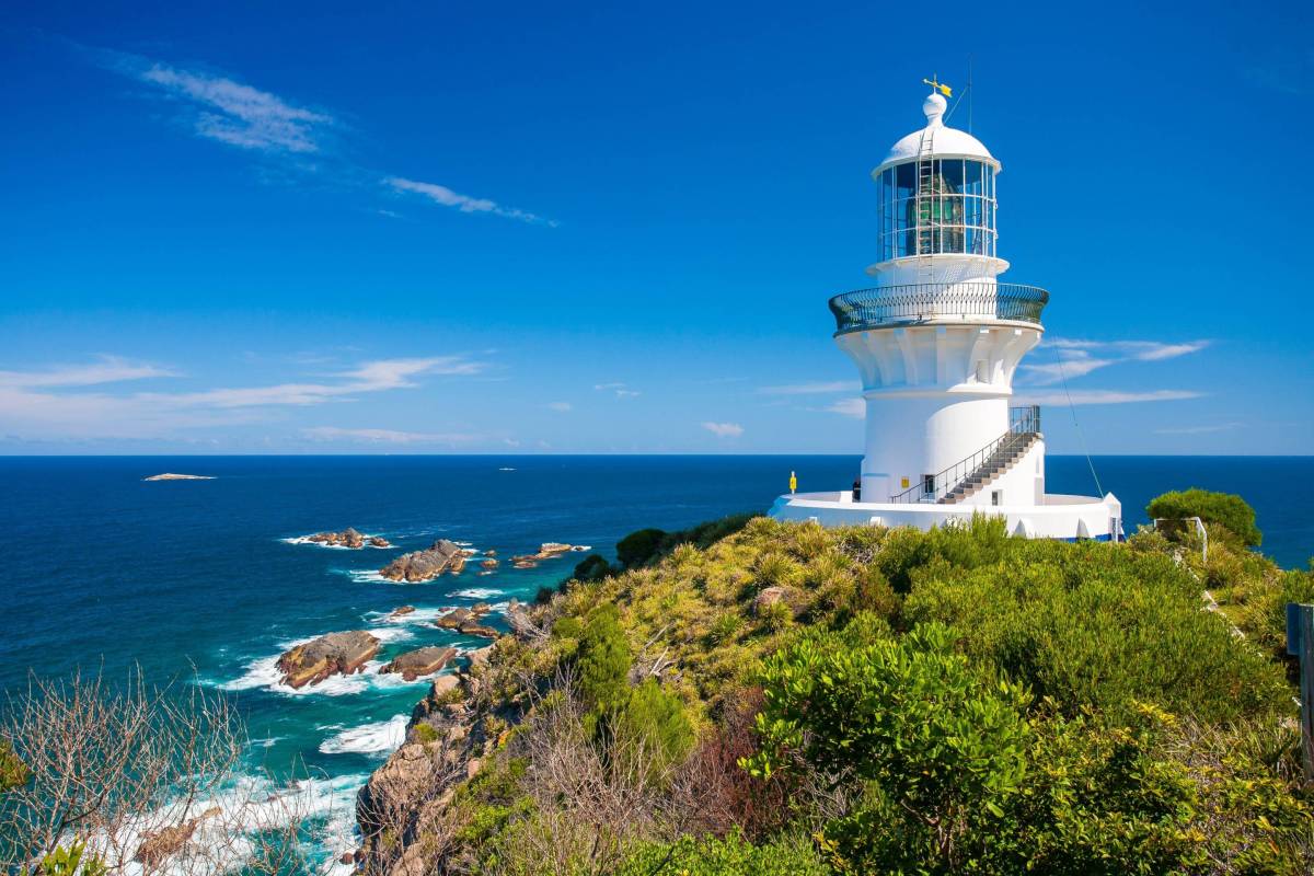Aerial view of Sugarloaf Point Lighthouse perched on a rugged headland, surrounded by blue ocean and forested coastline at Seal Rocks