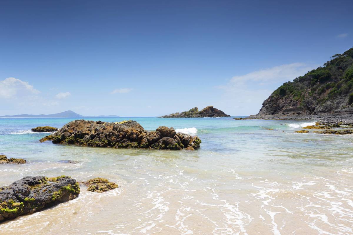 Clear turquoise water washing over a sandy beach dotted with rocky outcrops at Seal Rocks, NSW