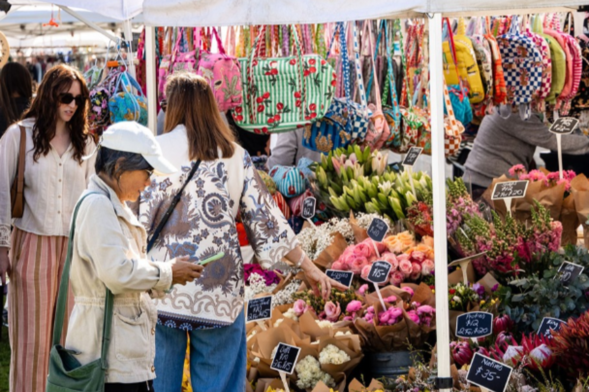 Shoppers browsing a colourful flower stall at a market event in Sydney, featuring bouquets of tulips, daffodils and other fresh flowers beneath white market tents