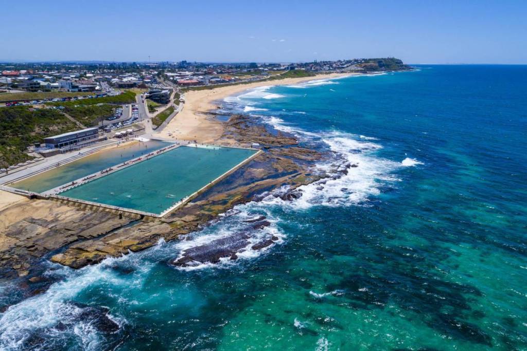 Aerial view of Merewether Ocean Baths, with turquoise swimming pools, rocky coastline and Merewether Beach stretching into the distance