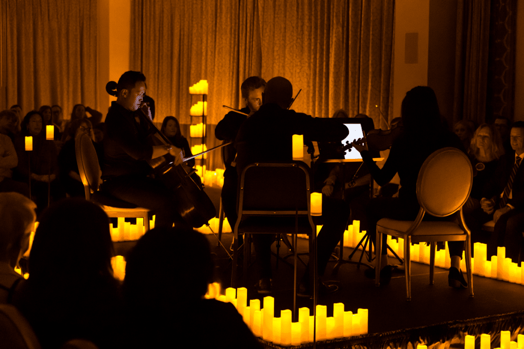The backs of a string quartet performing on a raised stage decorated with candles.