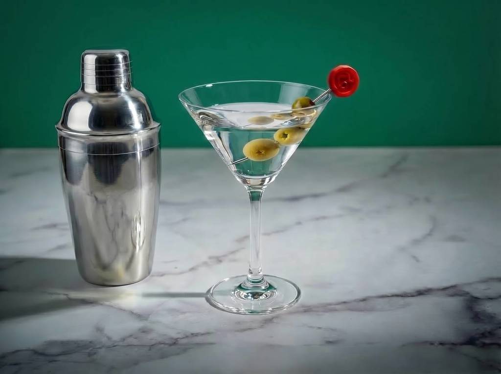a tanqueray martini with olives next to a cocktail shaker on a marble worktop