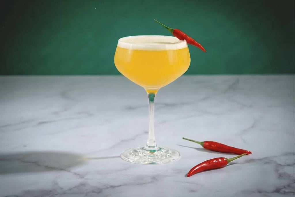 a tanqueray bees knees cocktail on a marble worktop garnished with chilli