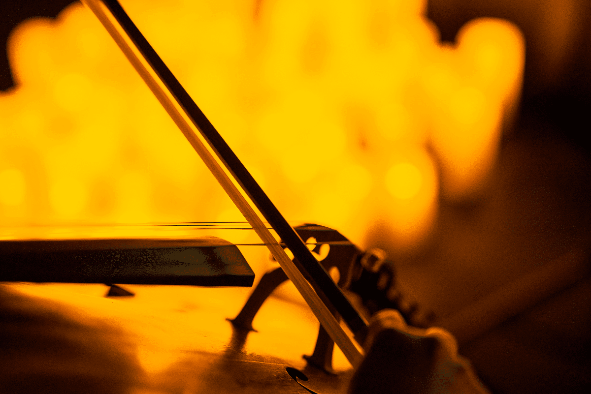 A close up of a bow playing a string instrument with the blurry glow of candles in the background.