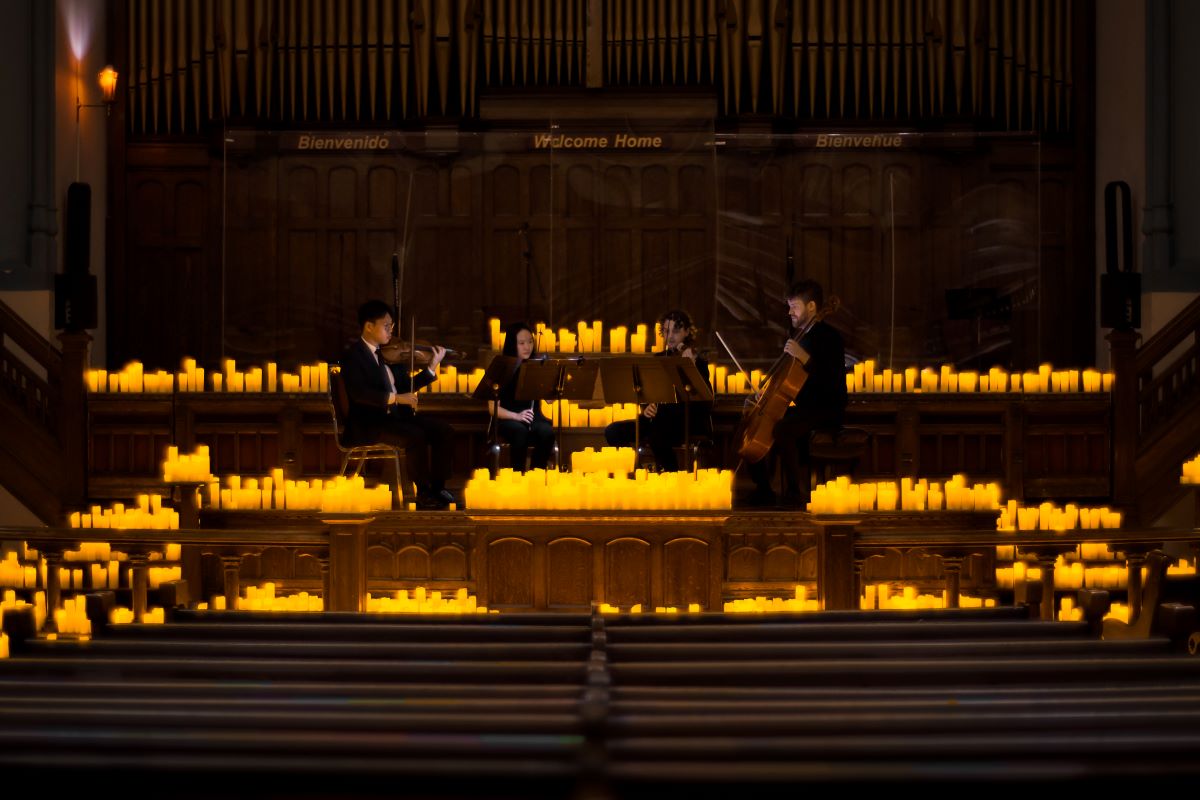 A string quartet performing on a candlelit stage at the Metropolitan Community Church of Toronto.
