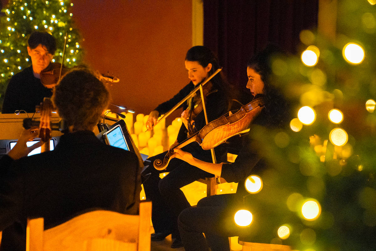 Integrantes de un cuarteto de cuerda tocando en un concierto Candlelight Navidad entre velas y árboles de Navidad