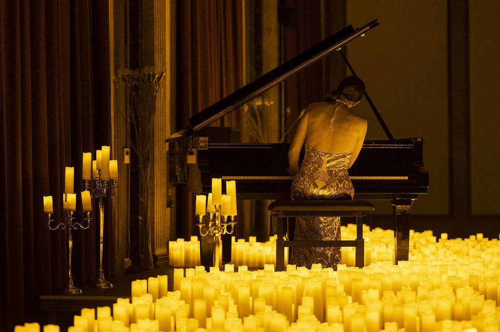 Un pianiste interprète une chanson assis au piano sur une scène éclairée à la bougie lors d'un concert Candlelight.