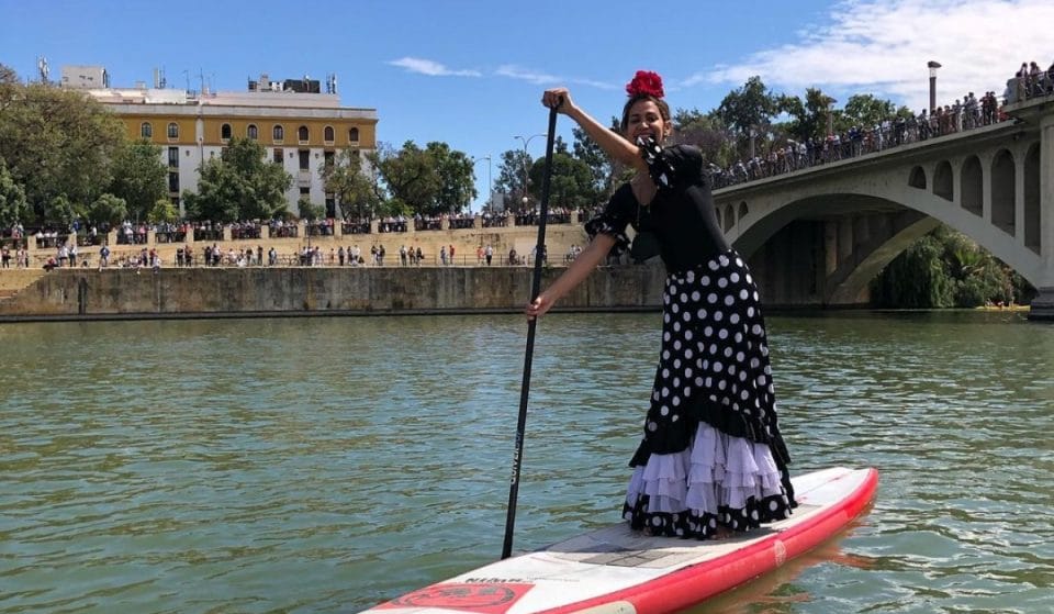 Una mujer vestida de flamenca recorre el Guadalquivir haciendo paddle surf