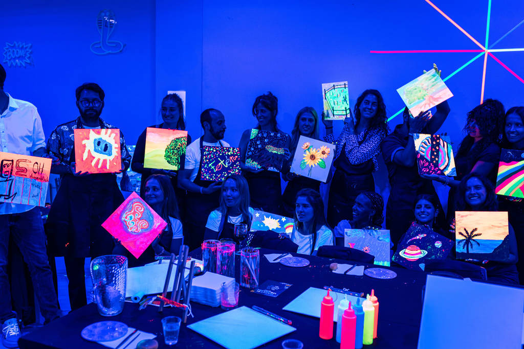 Grupo de personas enseñando sus obras creadas con pinturas neón en la oscuridad.