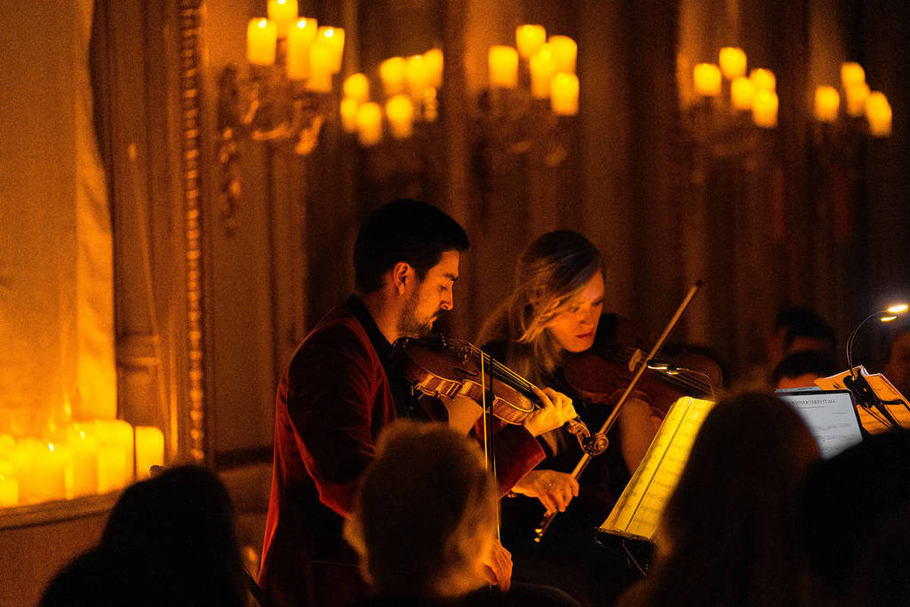 Dos músicos tocan en un cuarteto de cuerda durante un concierto Candlelight. Sobre ellos, muchas velas Candlelight.