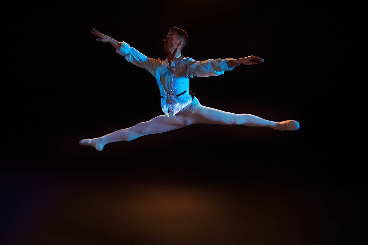 Un bailarín con un traje iluminado hace una acrobacia en el aire en Ballet of Lights.