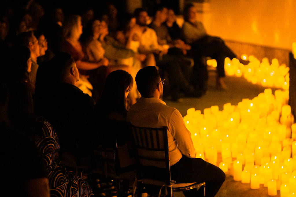 Varios espectadores miran atentos hacia un escenario cubierto de velas durante un concierto Candlelight.