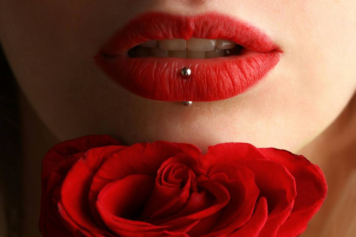 frau mit lippen piercing hält rote rose