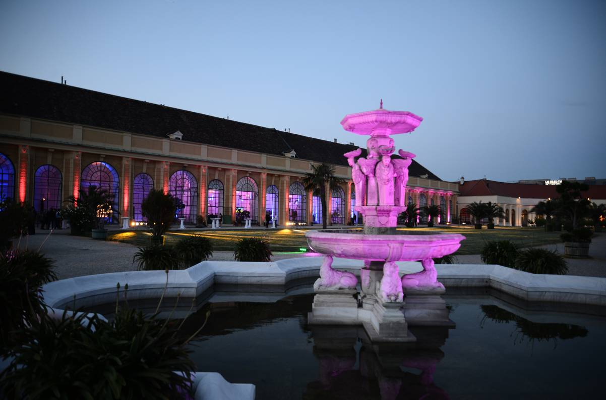 Außenansicht der Orangerie des Schloss Schönbrunn in Wien bei Dämmerung, Brunnen mit bunten Lichtern beleuchtet