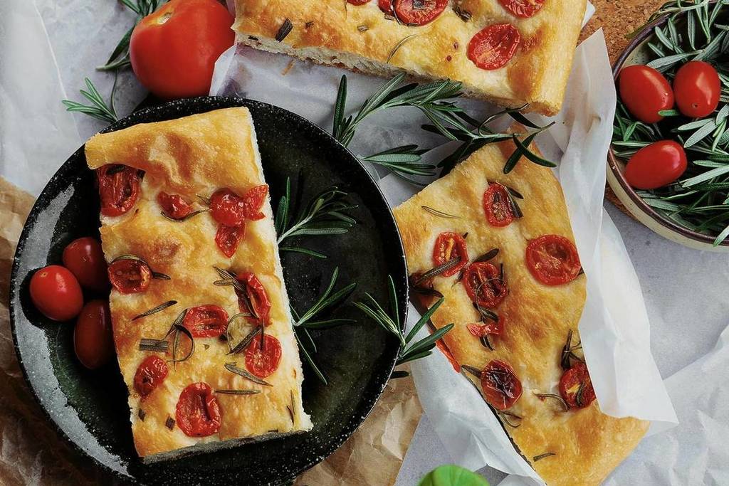 Focaccia auf einem Teller mit Tomaten und Rosmarin ästhetisch platziert
