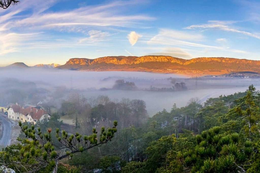 Malerischer Panoramablick auf das beschauliche Dorf Muthmannsdorf, das teilweise in Nebel gehüllt ist, während im Hintergrund das langgestreckte Felsmassiv der Hohen Wand im warmen Sonnenlicht leuchtet.
