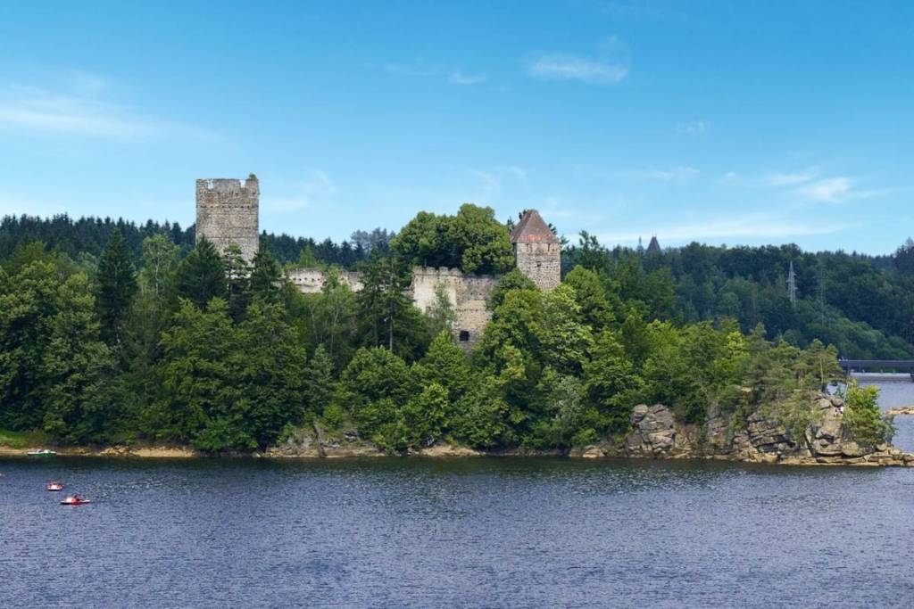 Das blaue Wasser des Stausees Ottenstein an einem sonnigen Tag. Auf einer bewaldeten Halbinsel thront die historische Ruine Lichtenfels, während im Vordergrund kleine Boote auf dem Wasser treiben.